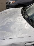 Silver car with a lot of hail dings on hood.