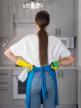 Woman wearing cleaning gloves and apron holding spray bottle. Has her hands on her hips.
