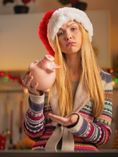 Woman in Santa hat looking sad in front of piggy bank.