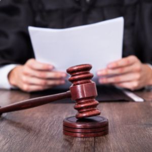 Judge's hands holding paper in background, gavel in foreground.