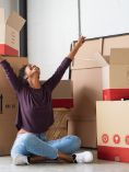 Excited woman sitting on the floor with packing boxes behind her