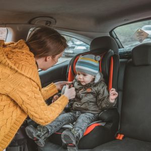 A mom putting a baby with a winter coat on in a car seat.
